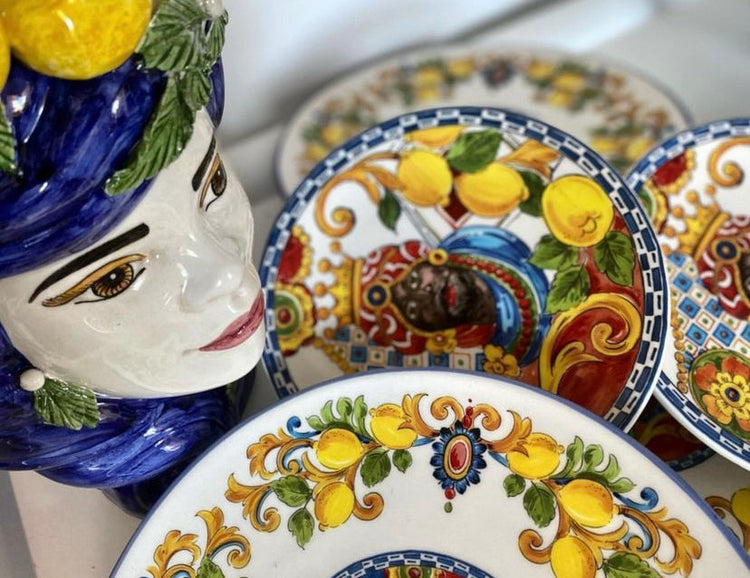 Dettaglio di piatti decorativi colorati con motivi mediterranei e volto in ceramica siciliana