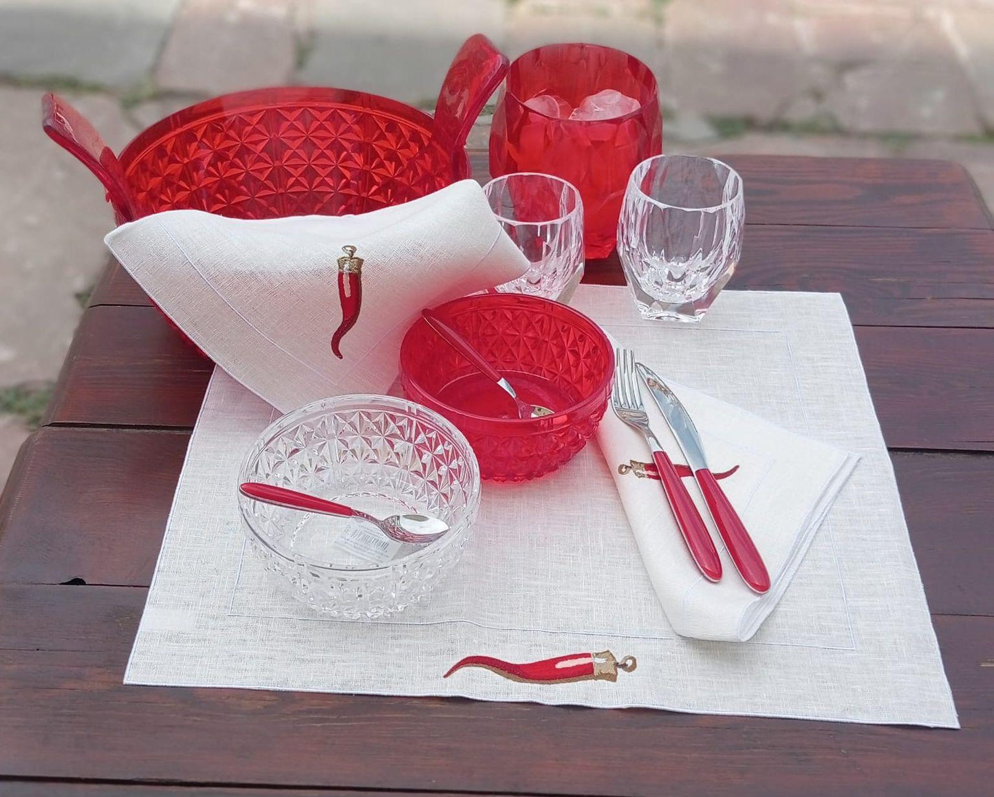 mise en place estiva con set americano e tovagliolo in lino cerato ricamato con corno portafortuna, bicchieri e ciotole in acrilico rosso e trasparente Mario Luca Giusti