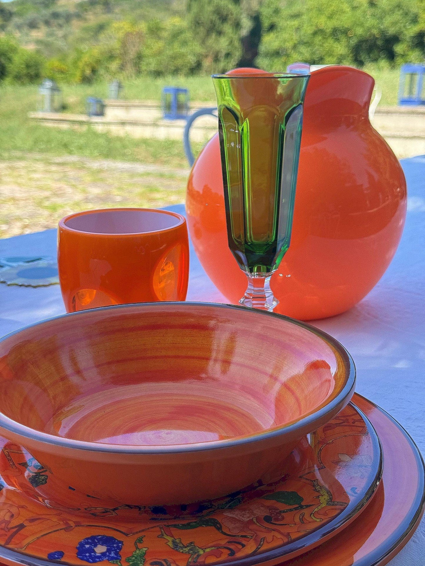 Piatto fondo Saint Tropez, piatto Pancale, bicchiere Fish Eye e Dolce Vita e brocca Palla arancio fluo Mario Luca Giusti su tavola estiva all'aperto