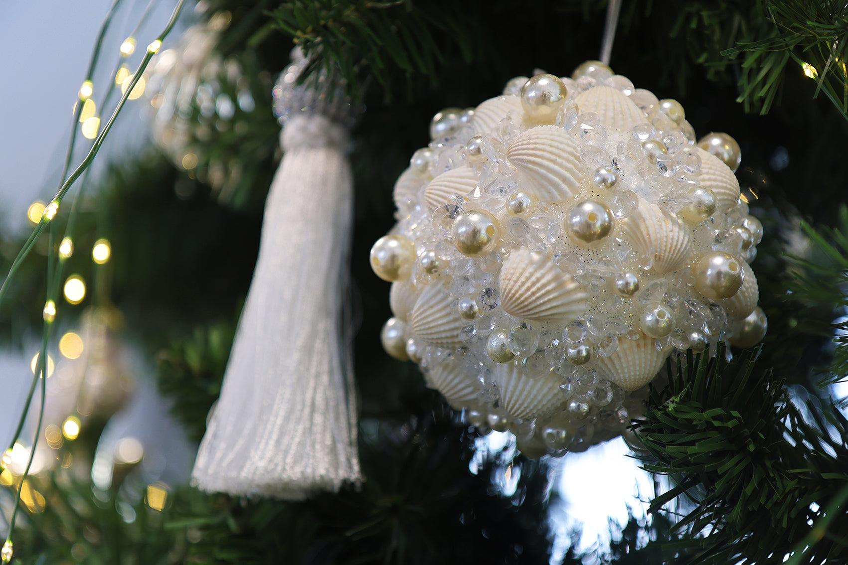 Decorazione Natale 2025: pallina artigianale con conchiglie, perle e cristalli su albero natalizio.