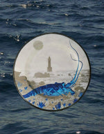 Piatto piano in melanina con motivo marino blu raffigurante una aragosta e ricci con faro e luna sullo sfondo fotografato su sfondo acqua