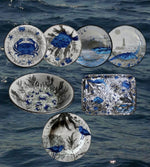 Set di piatti in melamina con decorazioni marine blu raffiguranti pesci granchi e coralli su sfondo illustrato a tema oceano e vassoio coordinato