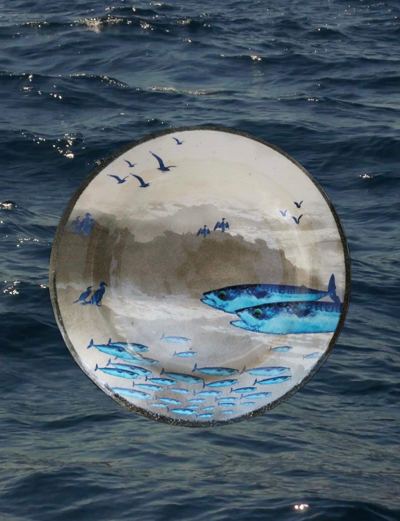 Piatto piano in melanina con motivo marino blu raffigurante delle sardine fotografato su sfondo acqua