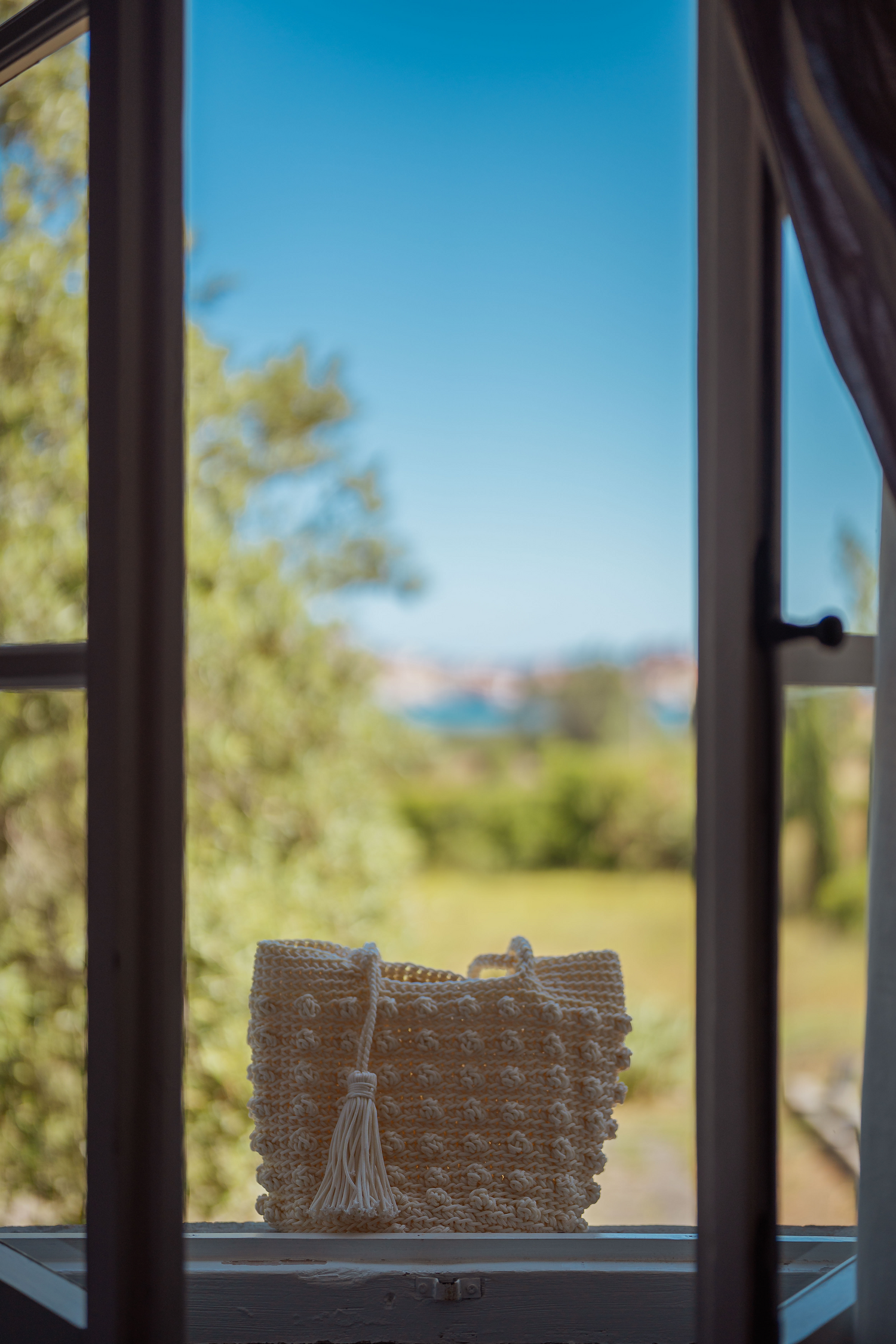 Borsa in corda intrecciata avorio con nappa decorativa appoggiata su finestra, Marika Selection