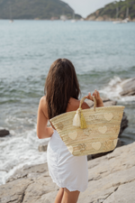 Borsa in paglia naturale con cuori ricamati e nappine decorative, indossata al mare, stile romantico estivo