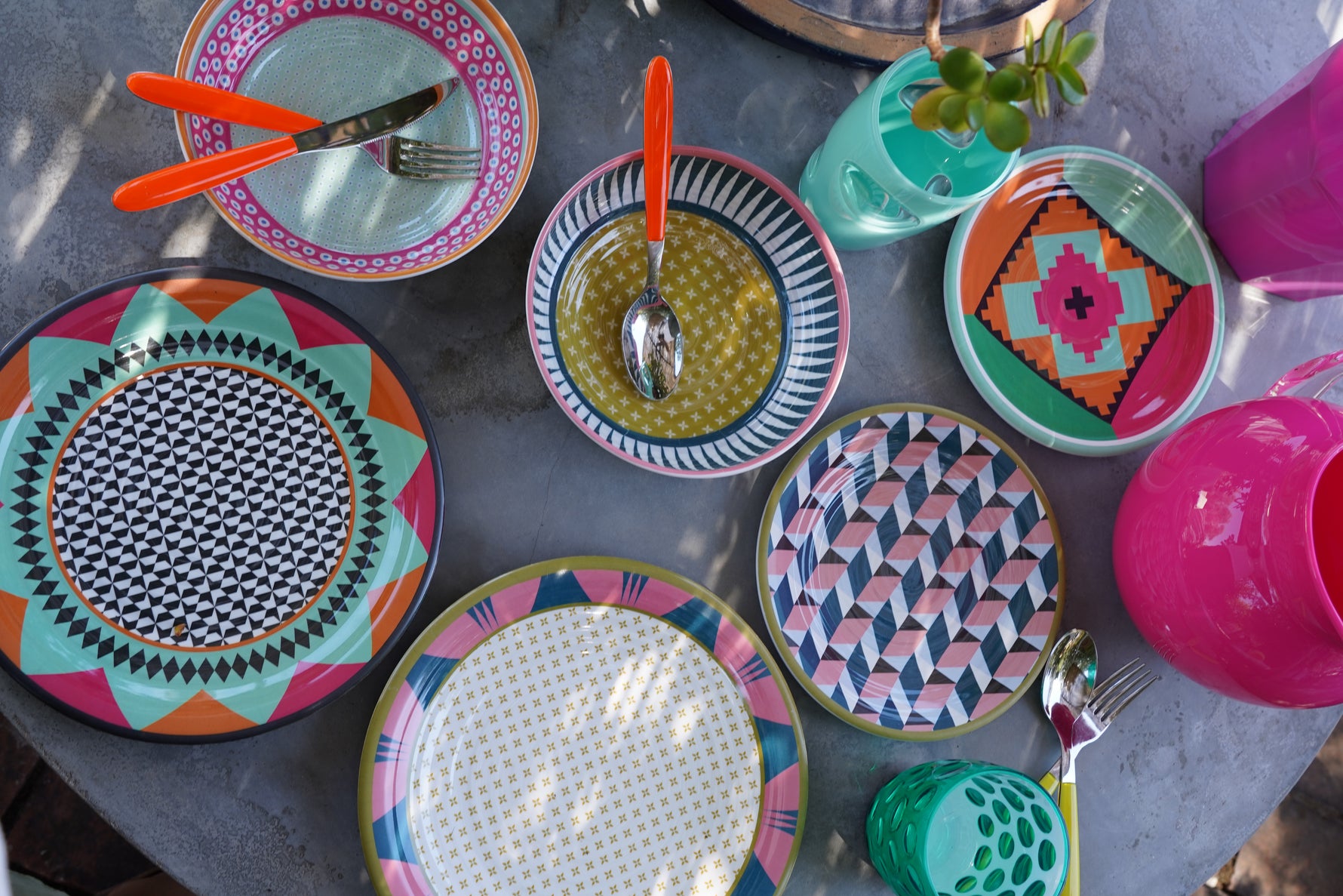Set piatti Modern Vesta in melamina con pattern geometrici colorati, tavola estiva vista dall’alto con bicchieri e accessori