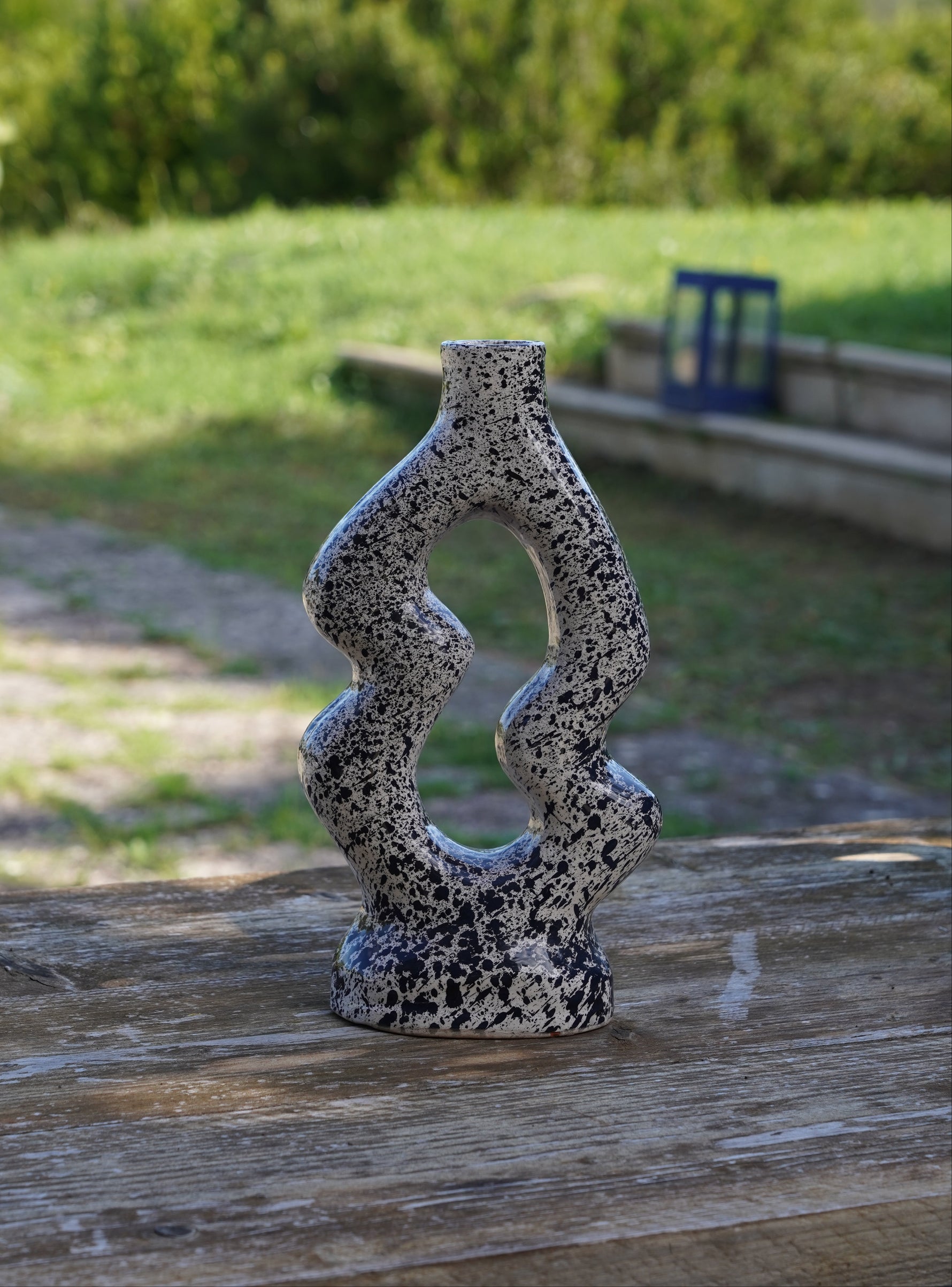 Vaso scultura artigianale in ceramica con finitura marmorizzata bianco e nero, fotografato all’aperto su tavolo in legno.