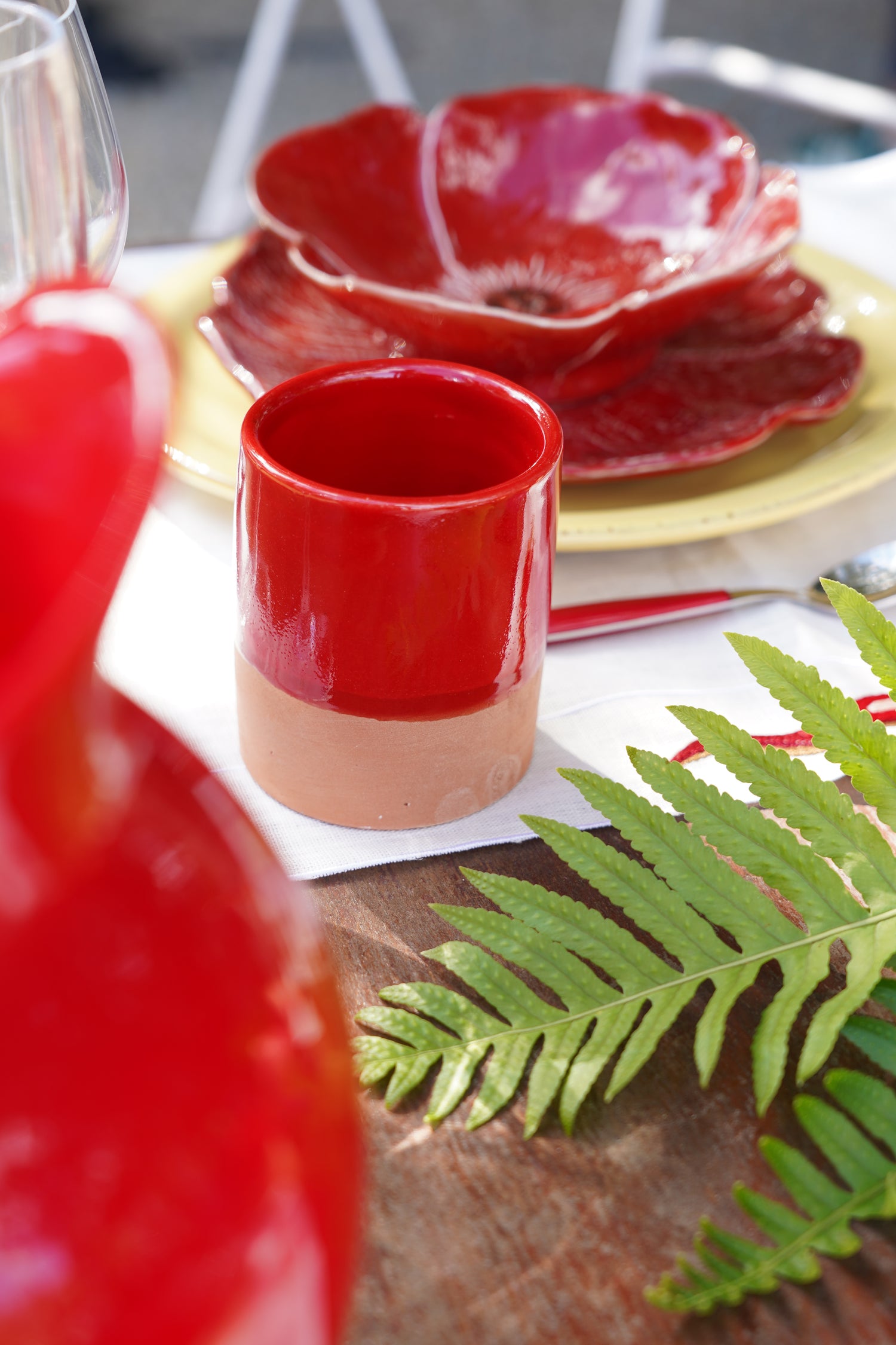 Tazzina in ceramica artigianale rossa con piatti coordinati su tavola apparecchiata all’aperto