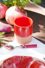 Tazzina in ceramica artigianale rossa con melagrane e cucchiaino su tavolo in legno