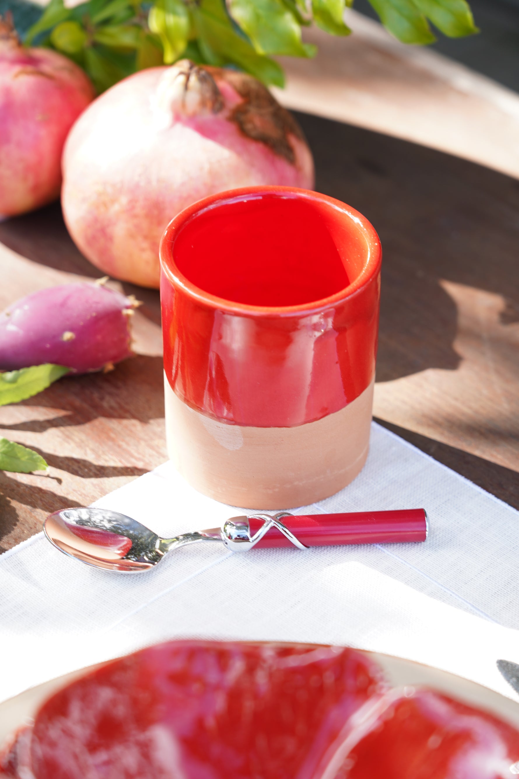 Tazzina in ceramica artigianale rossa con melagrane e cucchiaino su tavolo in legno