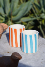 Set di bicchieri in ceramica artigianale a righe azzurre e arancioni su tavolo in pietra all’aperto