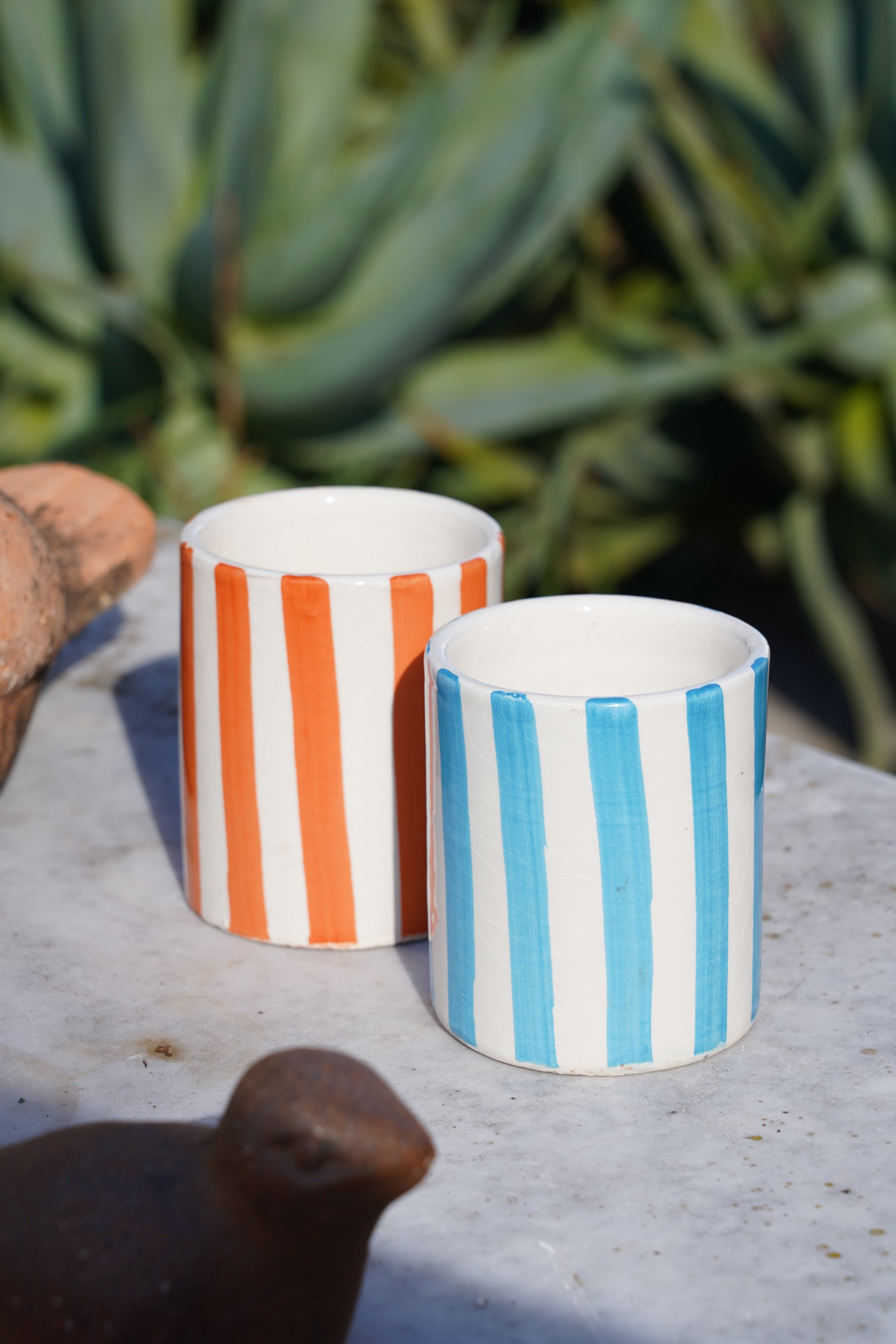 Set di bicchieri in ceramica artigianale a righe azzurre e arancioni su tavolo in pietra all’aperto