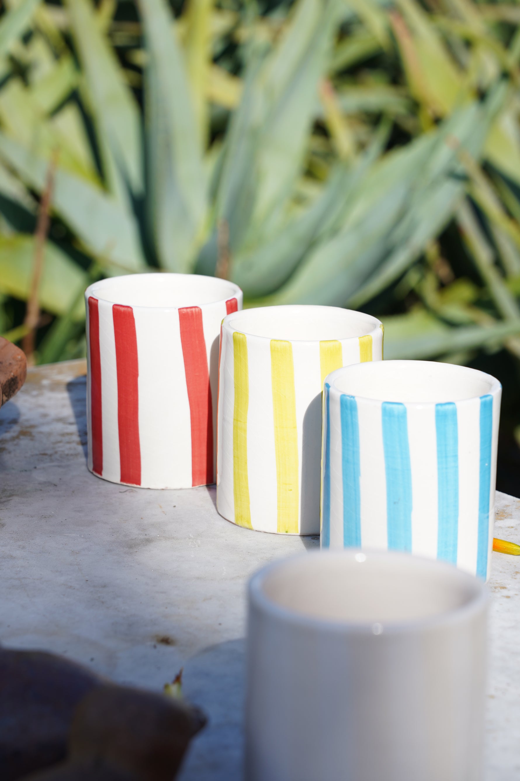 Set di bicchieri in ceramica artigianale a righe rosse, gialle e azzurrre su tavolo in pietra