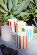 Collezione di bicchieri in ceramica artigianale a righe multicolore su tavolo in pietra all’aperto