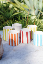 Set completo di bicchieri in ceramica artigianale a righe colorate su tavolo in pietra con piante sullo sfondo