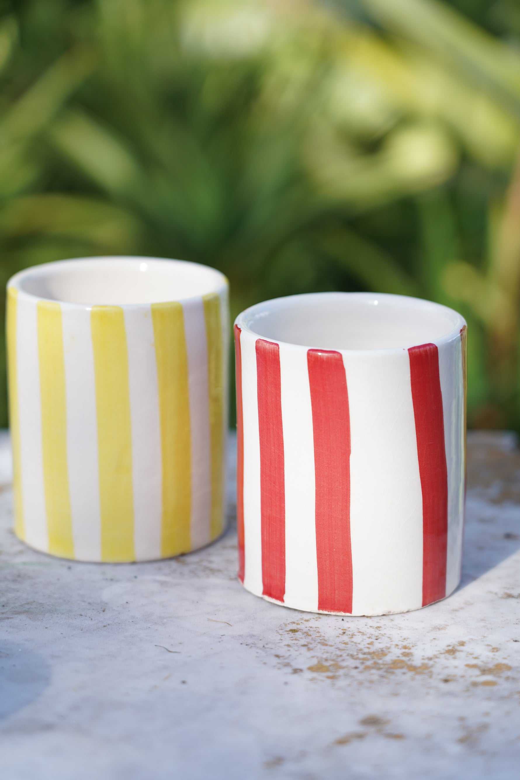 Bicchieri in ceramica artigianale a righe gialle e rosse su tavolo in pietra all’aperto