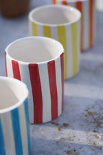 Linea di bicchieri in ceramica artigianale a righe colorate su tavolo in pietra all’aperto