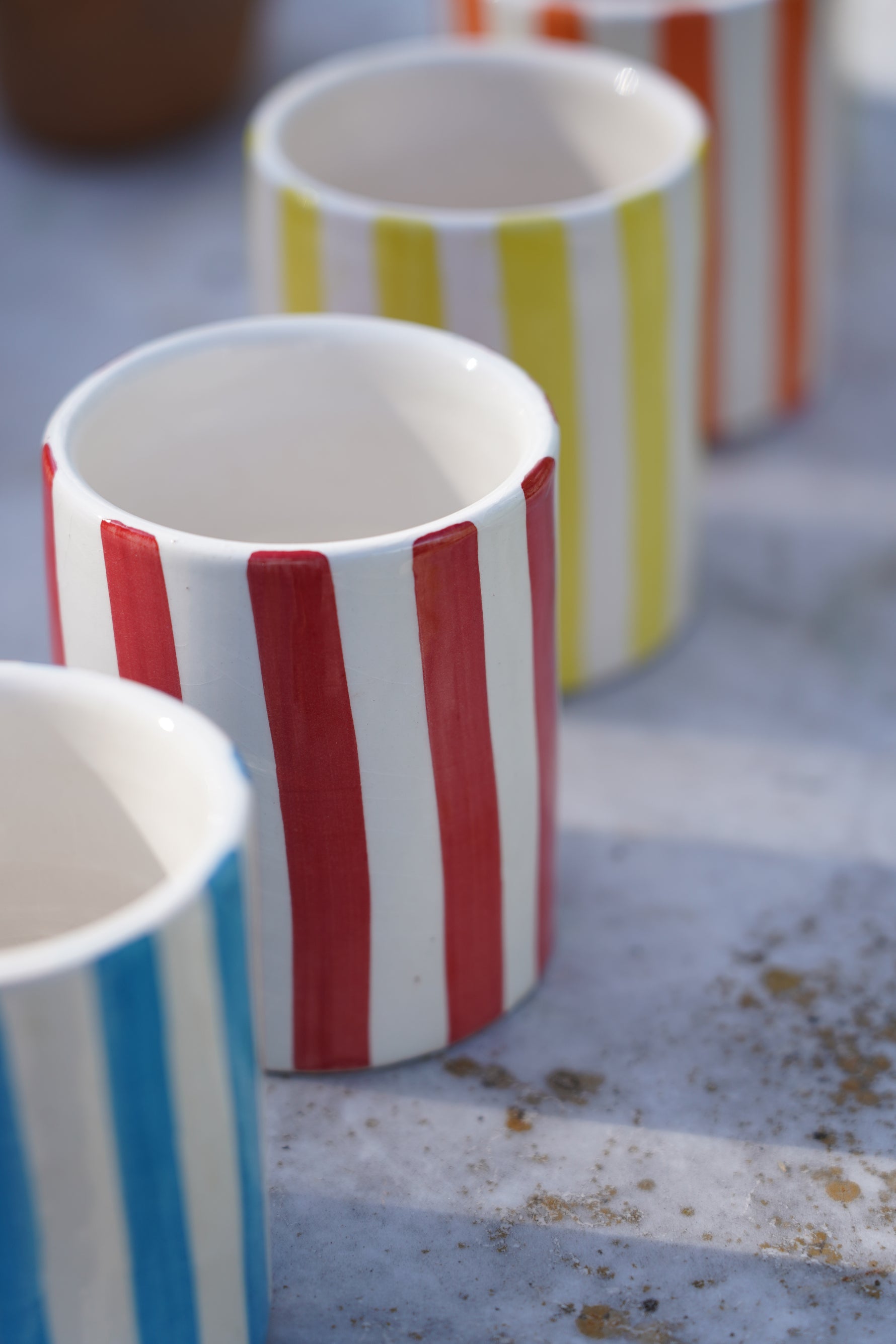 Linea di bicchieri in ceramica artigianale a righe colorate su tavolo in pietra all’aperto