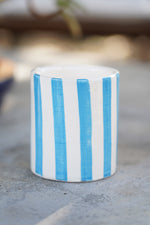 Bicchiere in ceramica artigianale a righe blu e bianche su superficie in pietr