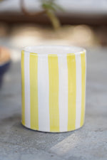 Bicchiere in ceramica artigianale a righe gialle e bianche su superficie in pietra