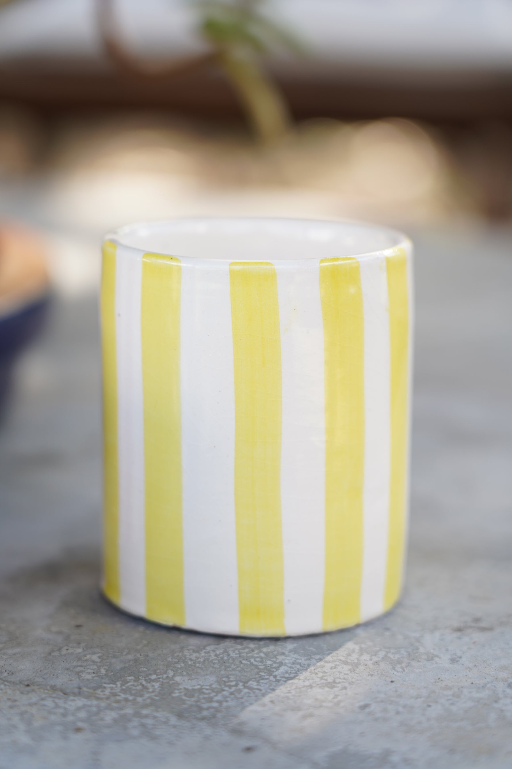 Bicchiere in ceramica artigianale a righe gialle e bianche su superficie in pietra