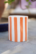 Set di bicchieri in ceramica artigianale a righe blu e arancioni su tavolo in pietra all’aperto