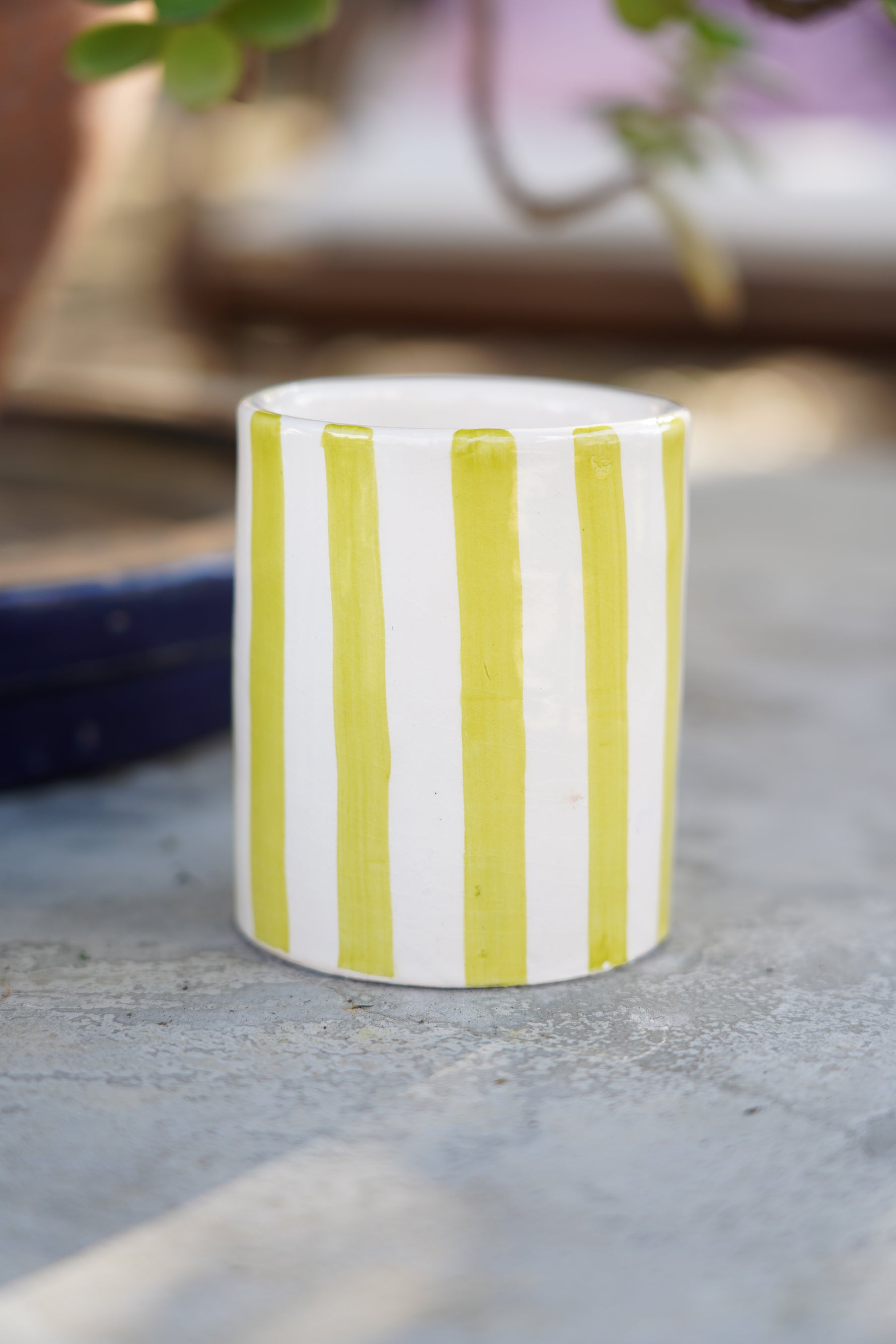 Bicchiere in ceramica artigianale a righe verde e bianche su tavolo in pietra con piante sullo sfondo