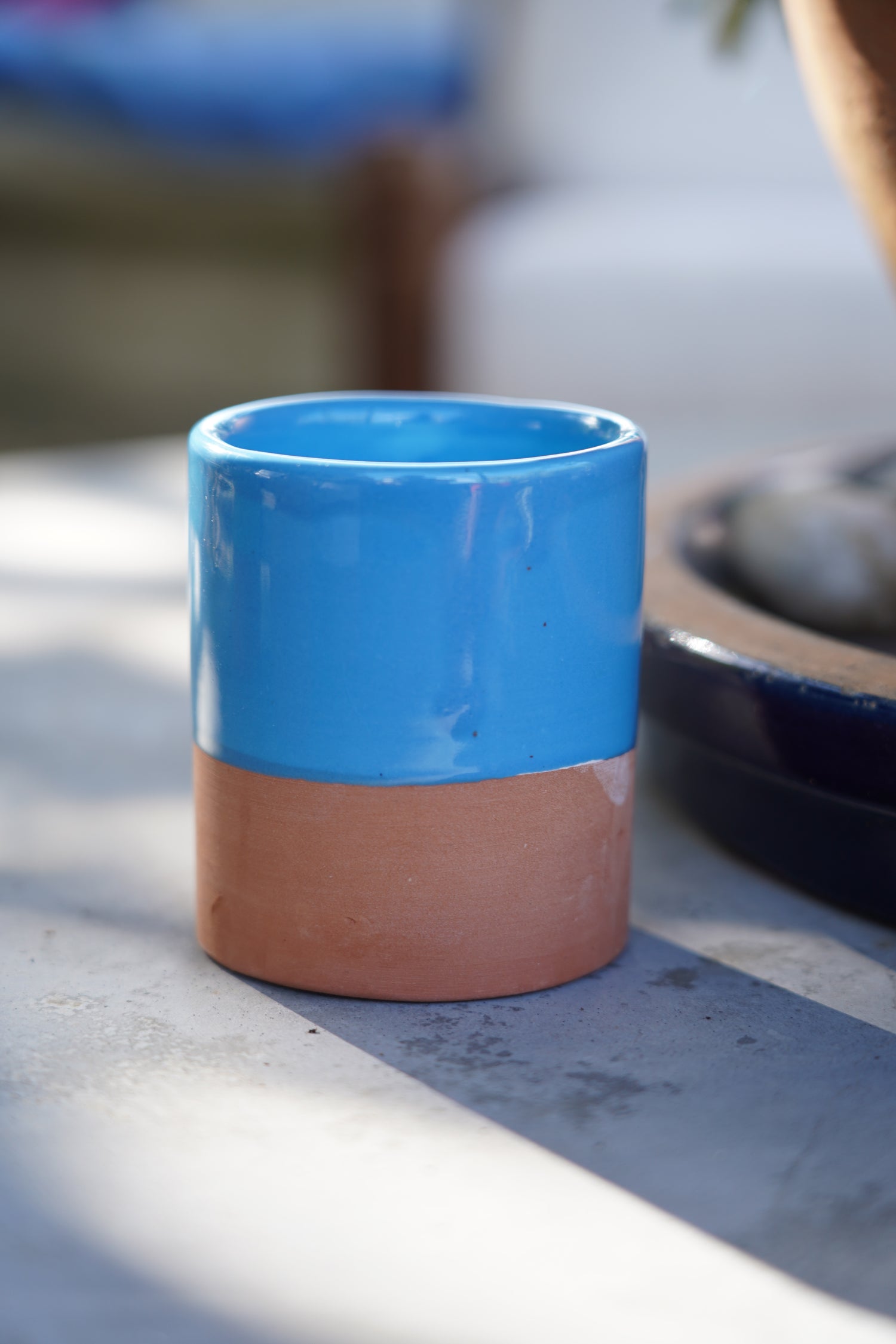 Tazzina in ceramica artigianale azzurra con base in terracotta su tavolo all’aperto