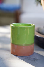 Tazzina in ceramica artigianale verde con base in terracotta su tavolo all’aperto