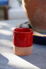 Tazzina in ceramica artigianale rossa con base in terracotta su tavolo all’aperto