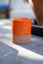 Tazzina in ceramica artigianale arancione con base in terracotta su tavolo all’aperto