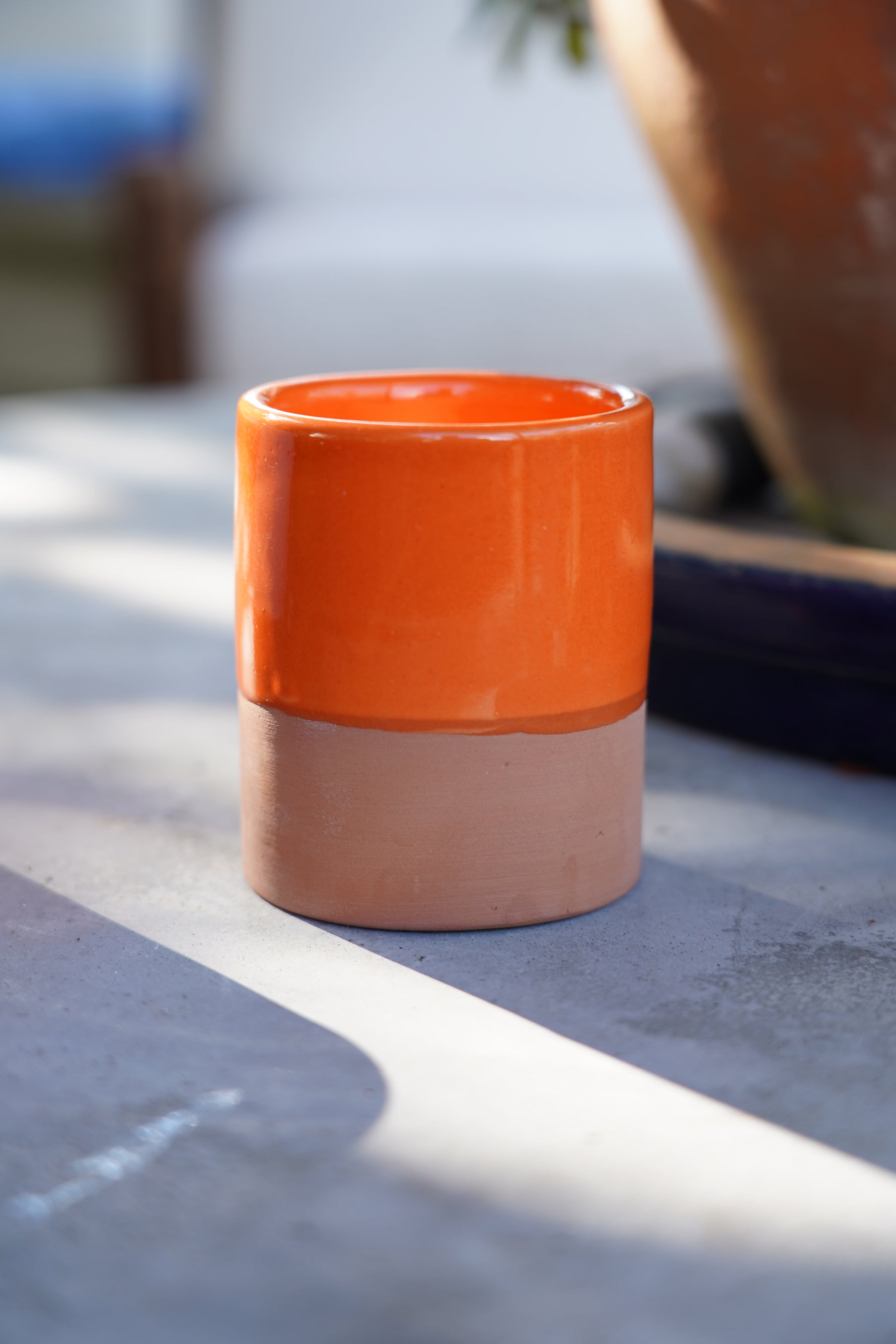 Tazzina in ceramica artigianale arancione con base in terracotta su tavolo all’aperto