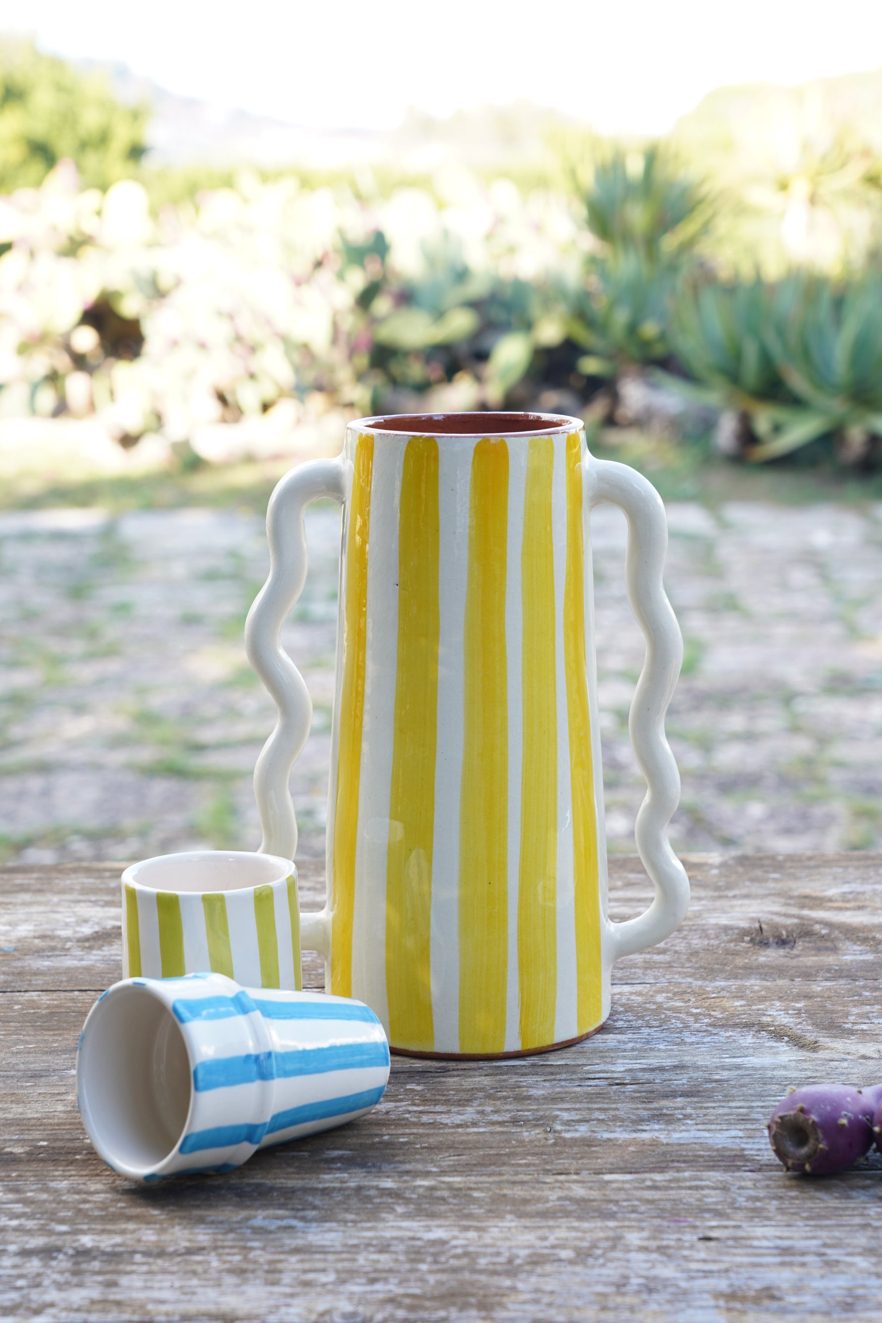 Vaso caraffa in ceramica fatto a mano con righe giallo e bianco, altezza 28 cm, con piccoli bicchieri artigianali su tavolo rustico