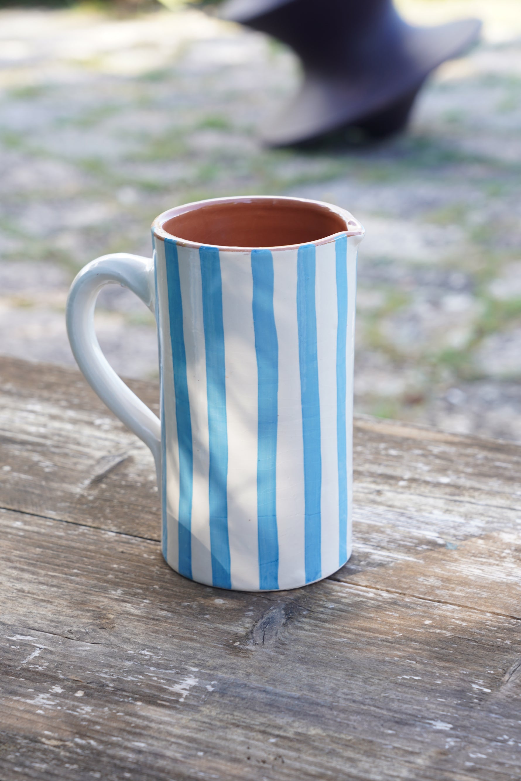 Vaso artigianale in ceramica a righe azzurre e bianche, altezza 19 cm, fatto a mano, appoggiato su tavolo in legno all’aperto