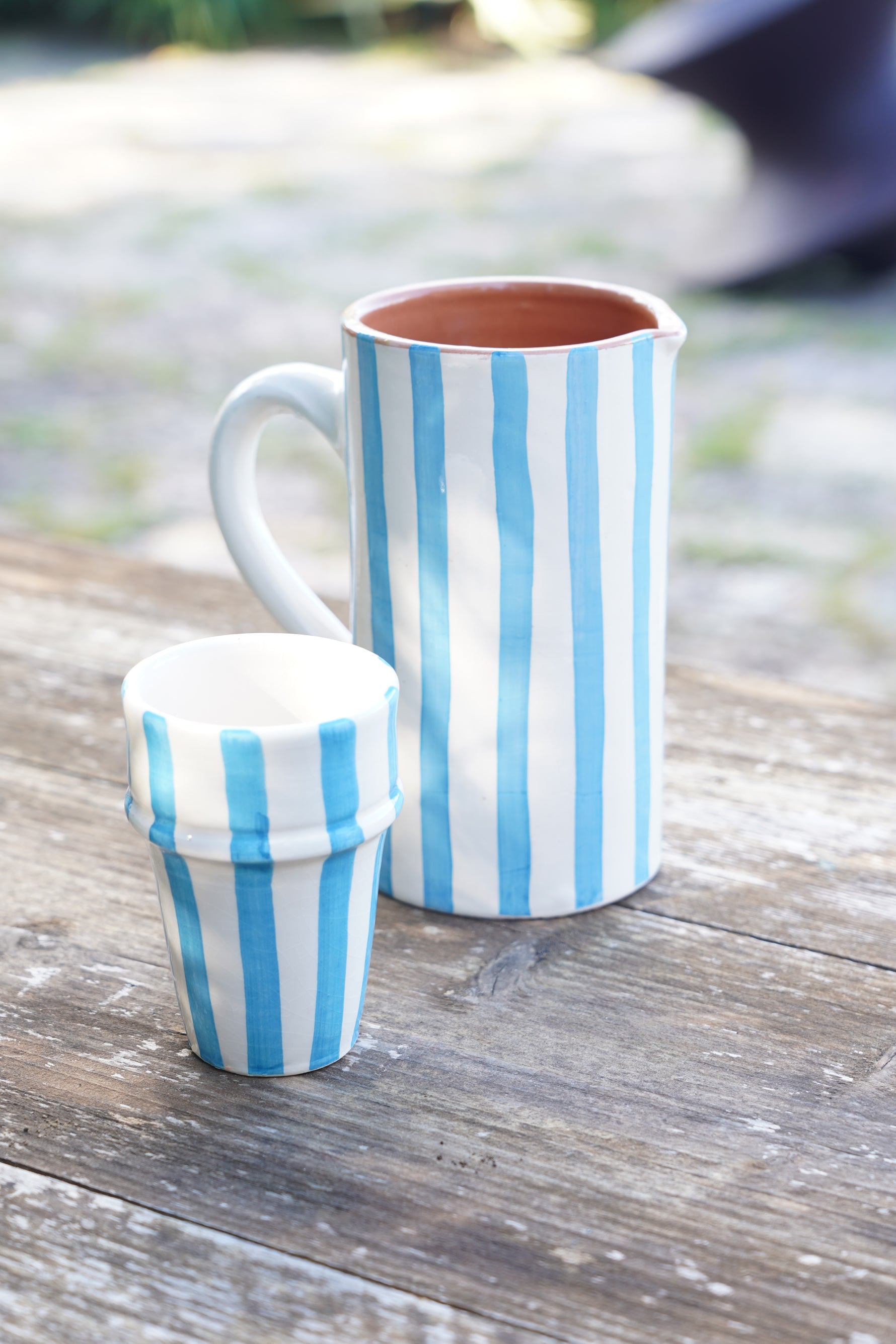 Caraffa e bicchiere coordinati in ceramica con righe azzurre verticali, stile artigianale, su tavolo in legno
