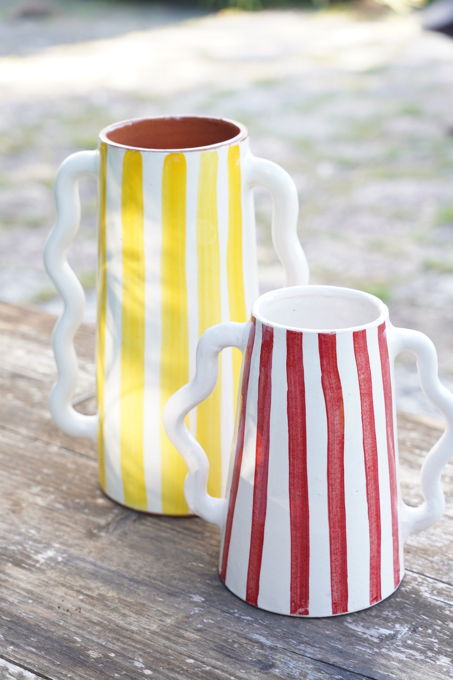 Brocche in ceramica a righe gialle e rosse con manici ondulati su tavolo in legno