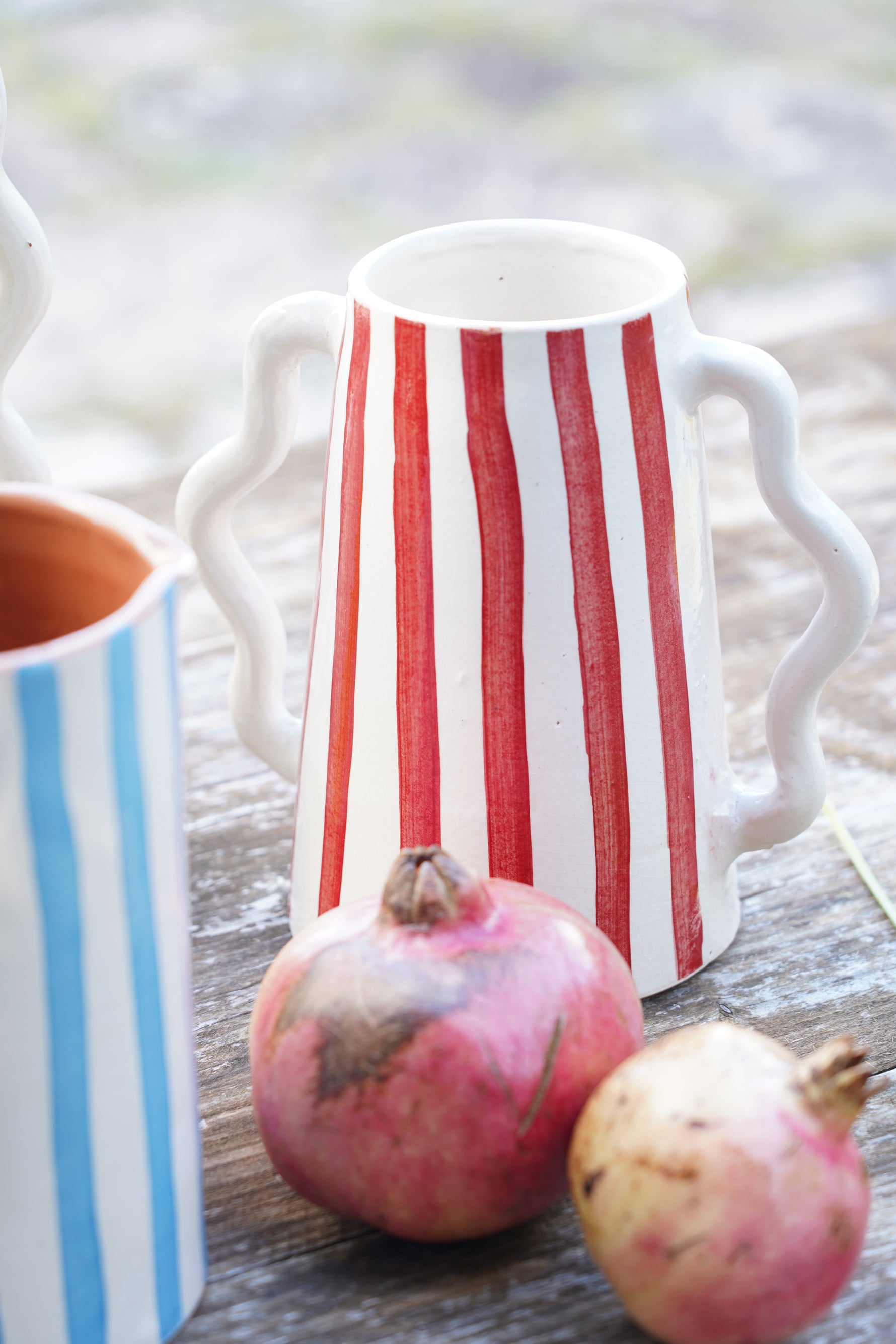 Brocca in ceramica artigianale a righe rosse con melagrane su tavolo in legno naturale