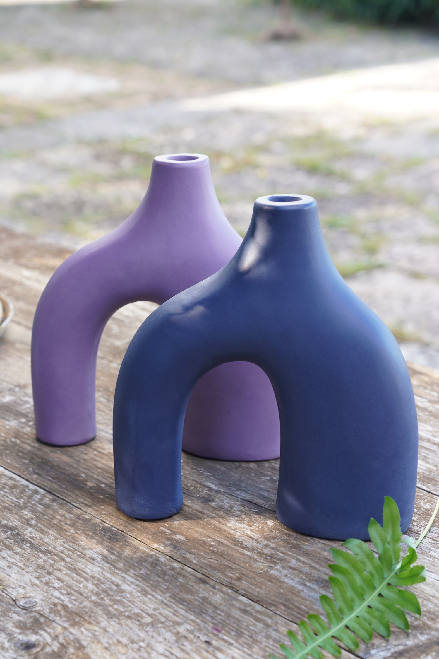 Vasi decorativi in ceramica opaca viola e blu dal design scultoreo su tavolo in legno all’aperto