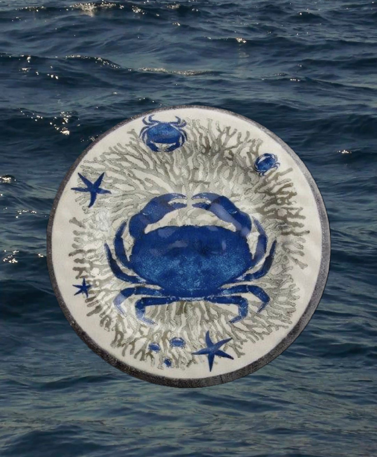 Piatto piano in melamina con decorazione marina blu, raffigurante un granchio e coralli, fotografato su sfondo acqua