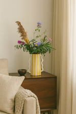 Vaso caraffa artigianale a righe gialle e bianche con fiori, h 28 cm, su mobile in legno in ambiente interno luminoso