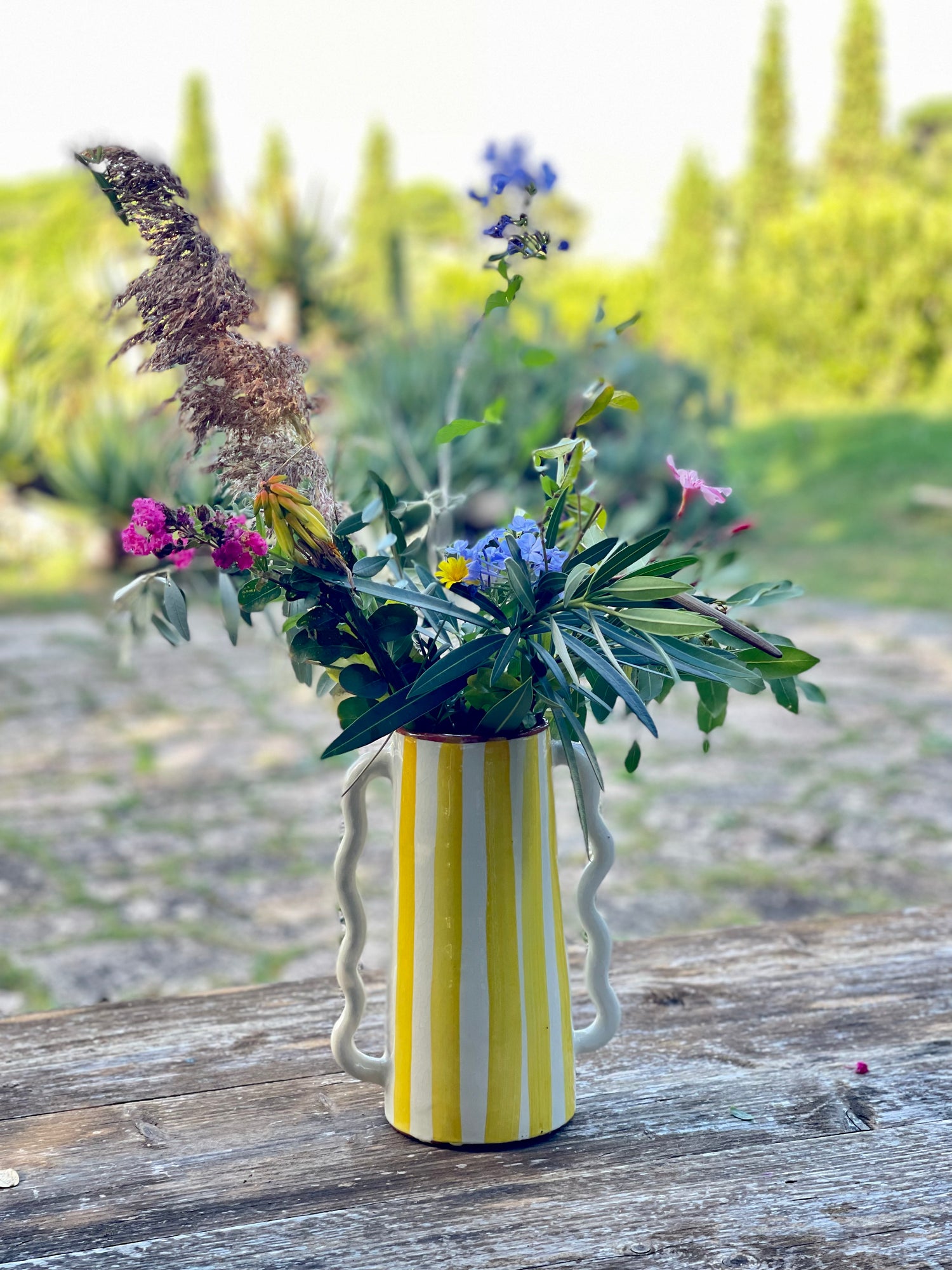 Vaso caraffa in ceramica giallo e bianco con composizione floreale, fatto a mano, su tavolo in legno in giardino