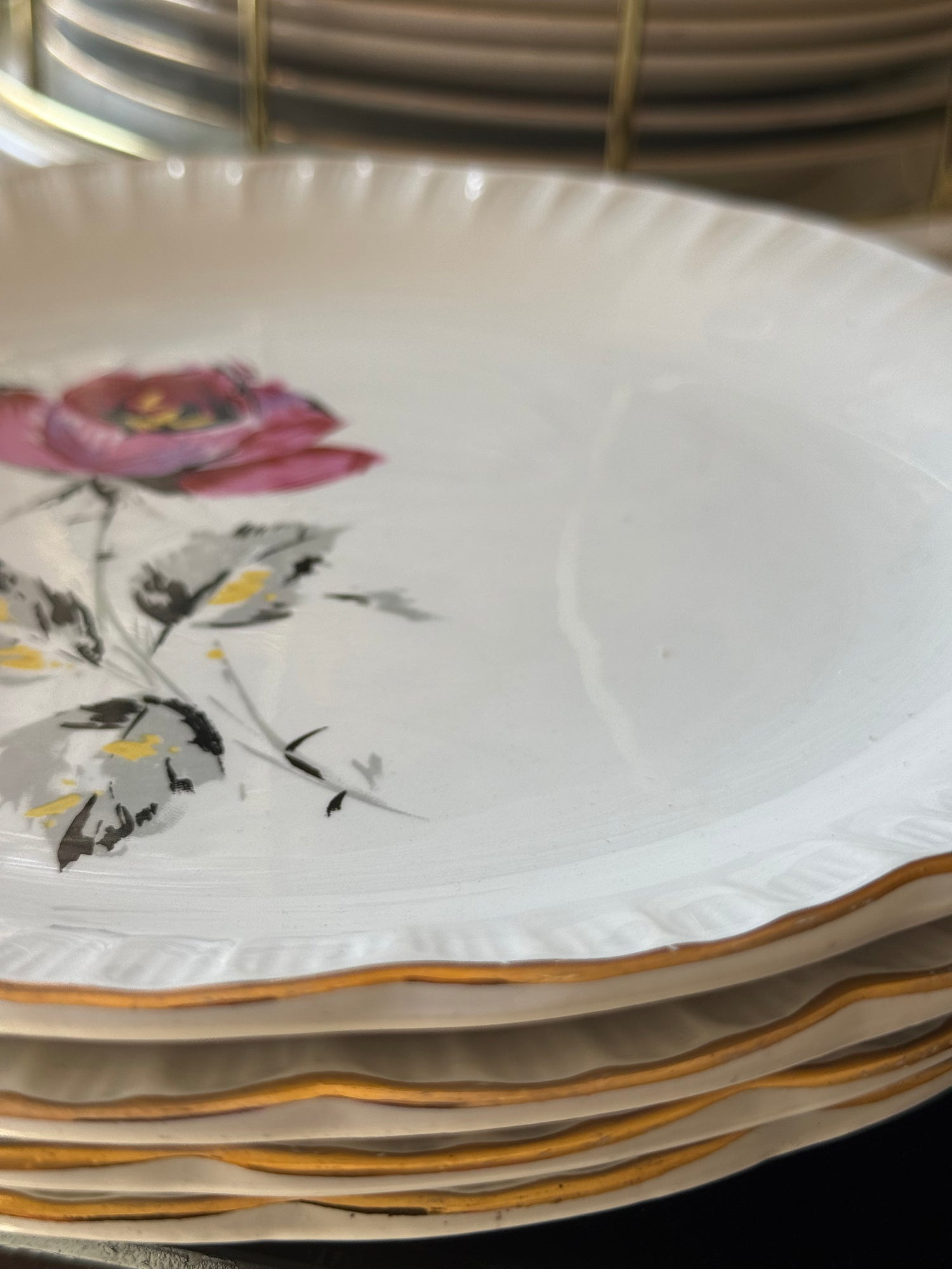 Dettaglio piatti vintage francesi in ceramica con bordo dorato ondulato e decoro floreale rosa
