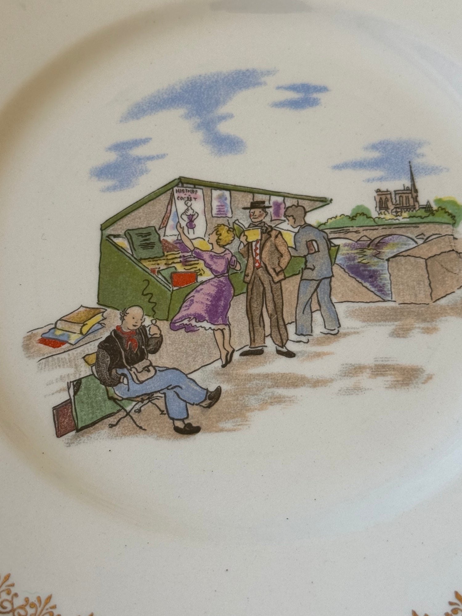 Particolare di piatto vintage decorativo con scena di bancarella d'arte sulla Senna, figure parigine e dettagli illustrati 