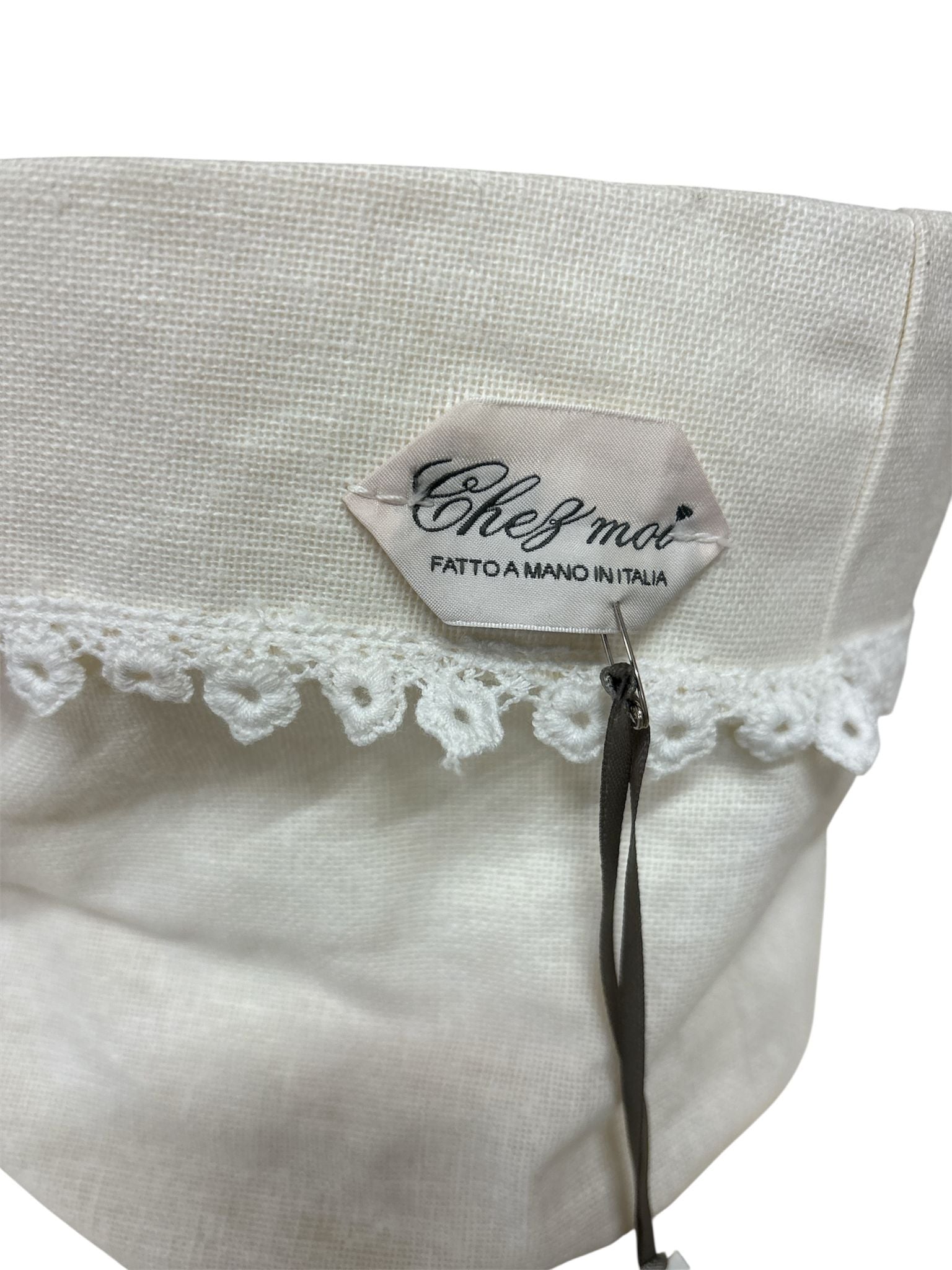 Dettaglio etichetta "Chez Moi fatto a manoi  in Italia" su cestino in lino con pizzo, artigianato italiano elegante.