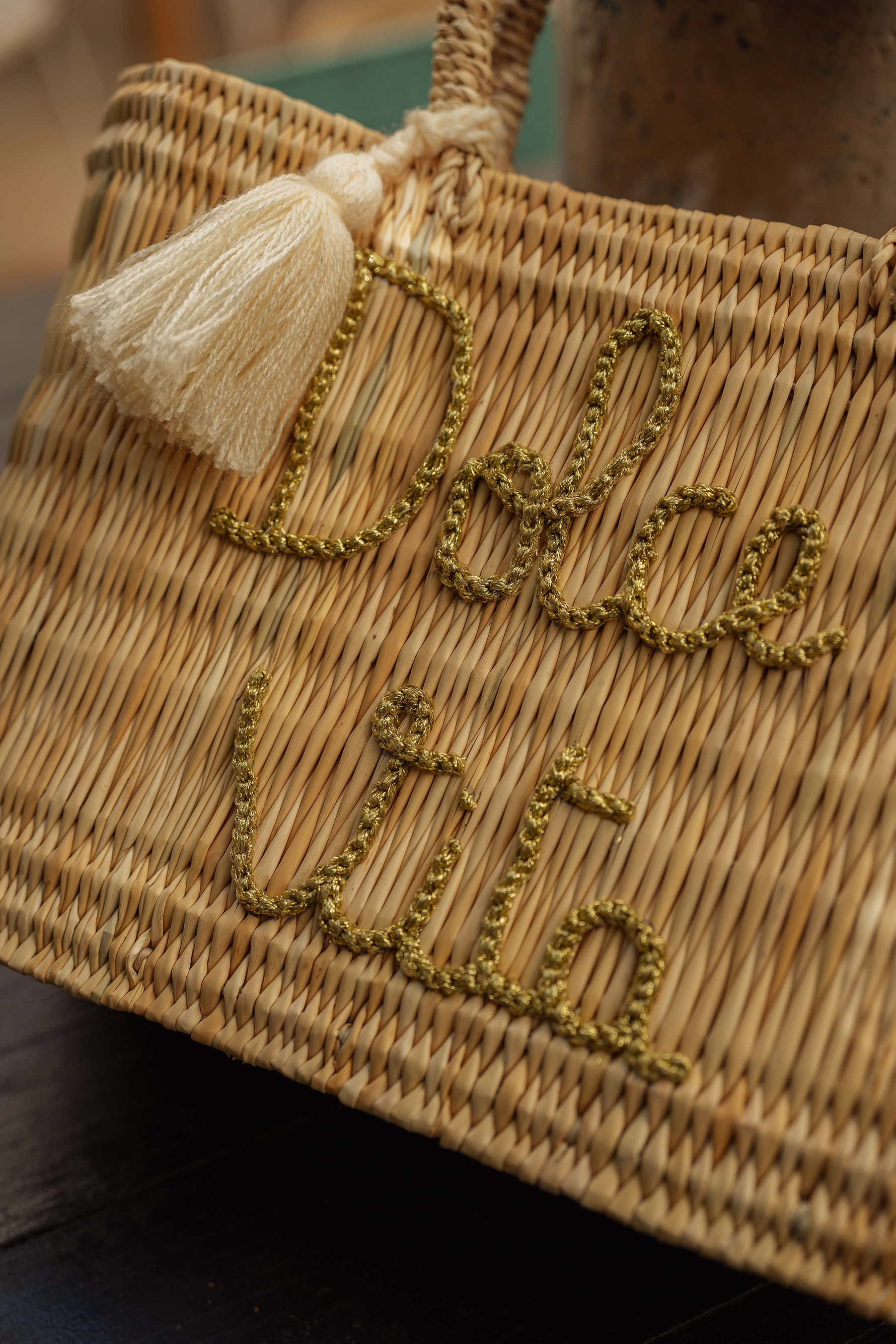 Dettaglio borsa in paglia con scritta Dolce Vita ricamata in filo dorato e nappa decorativa