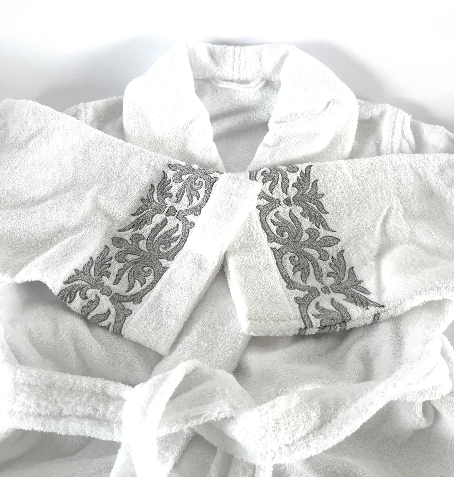 Accappatoio in spugna di lusso piegato, con ricamo grigio elegante sul bordo