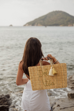 Borsa in paglia naturale con scritta Dolce Vita ricamata e nappine decorative, indossata al mare, stile mediterraneo estivo