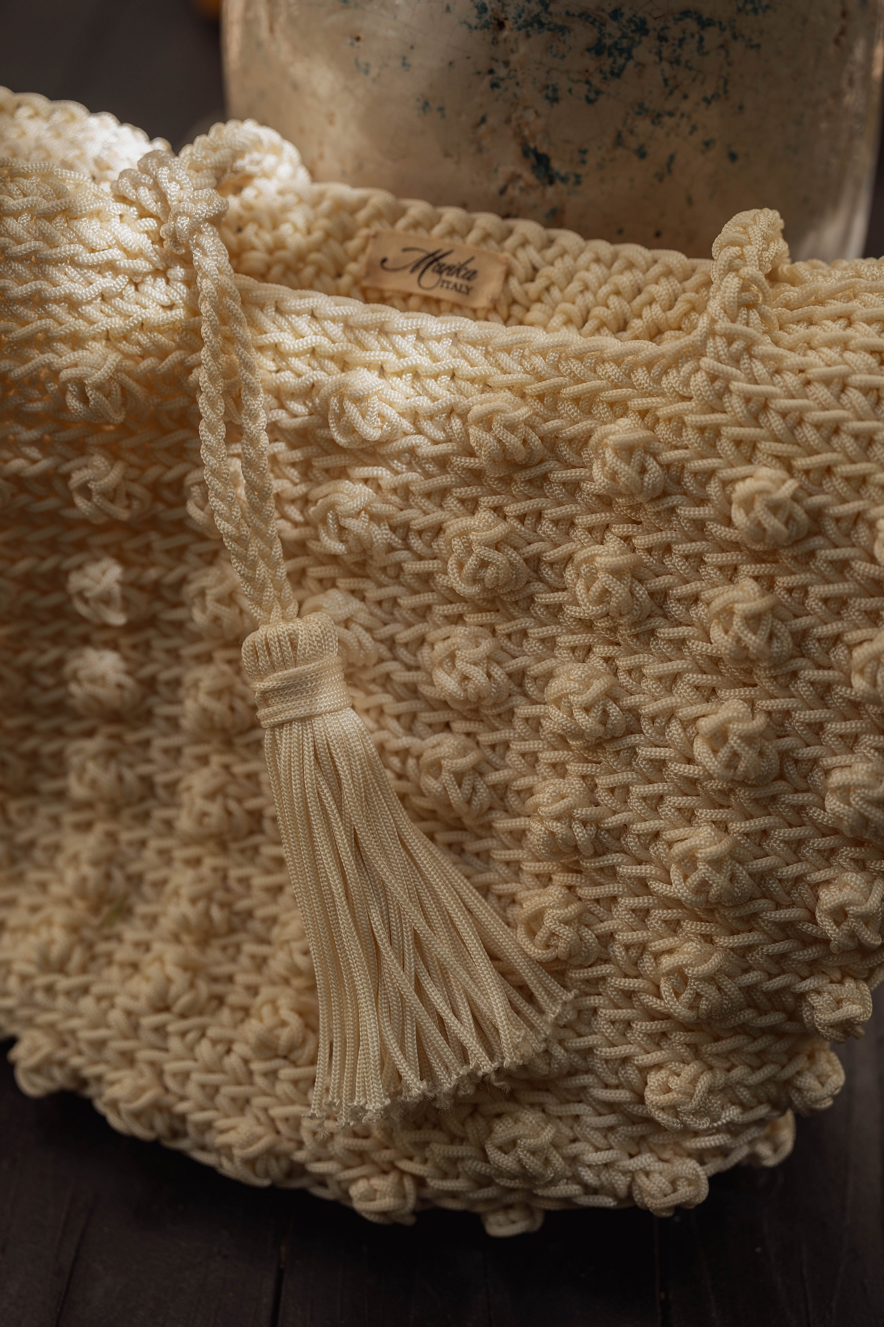 Dettaglio borsa in corda intrecciata con nodi in rilievo e nappa tono su tono, lavorazione artigianale