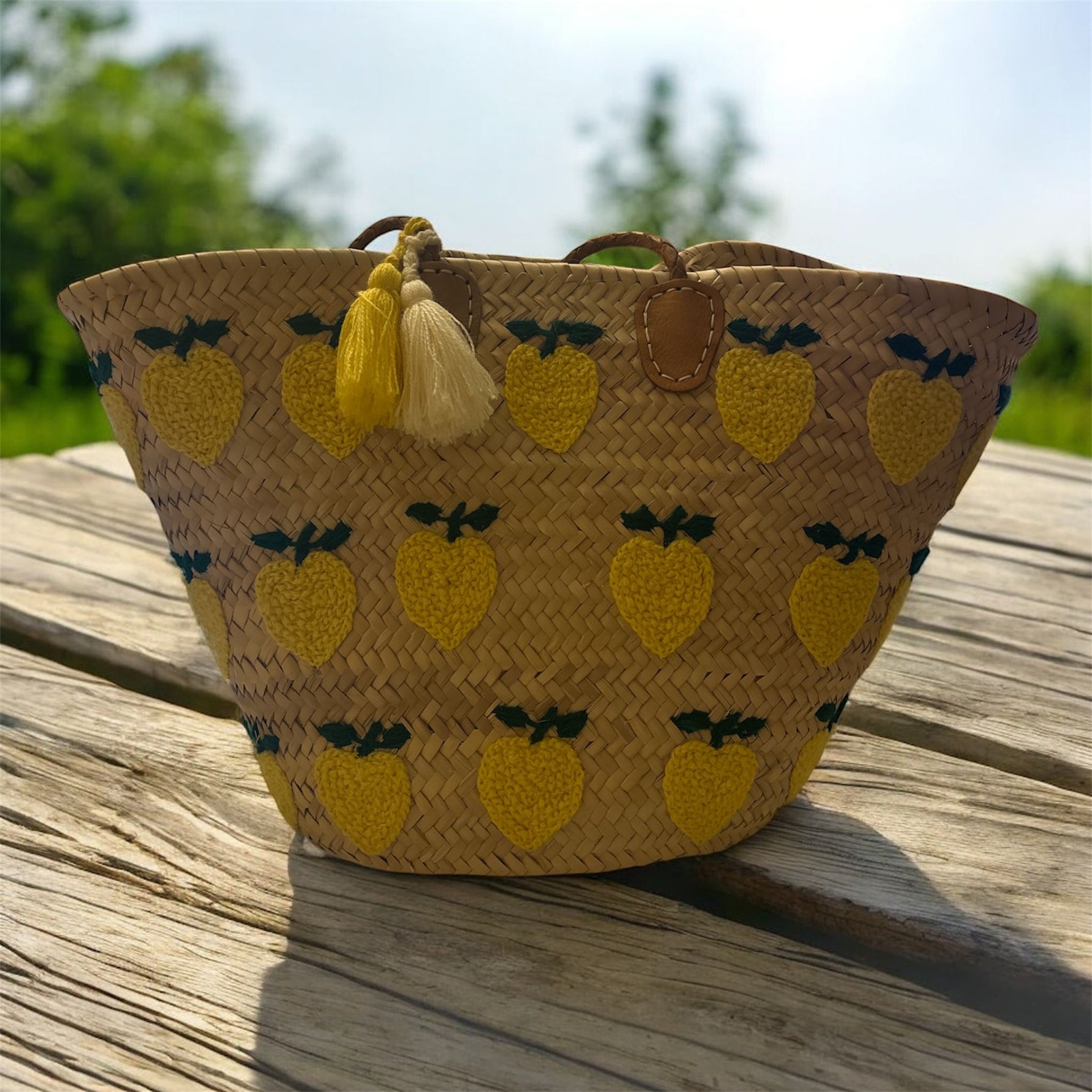 Borsa estiva in paglia con limoni ricamati appoggiata su tavolo in legno, stile mediterraneo Marika Selection

