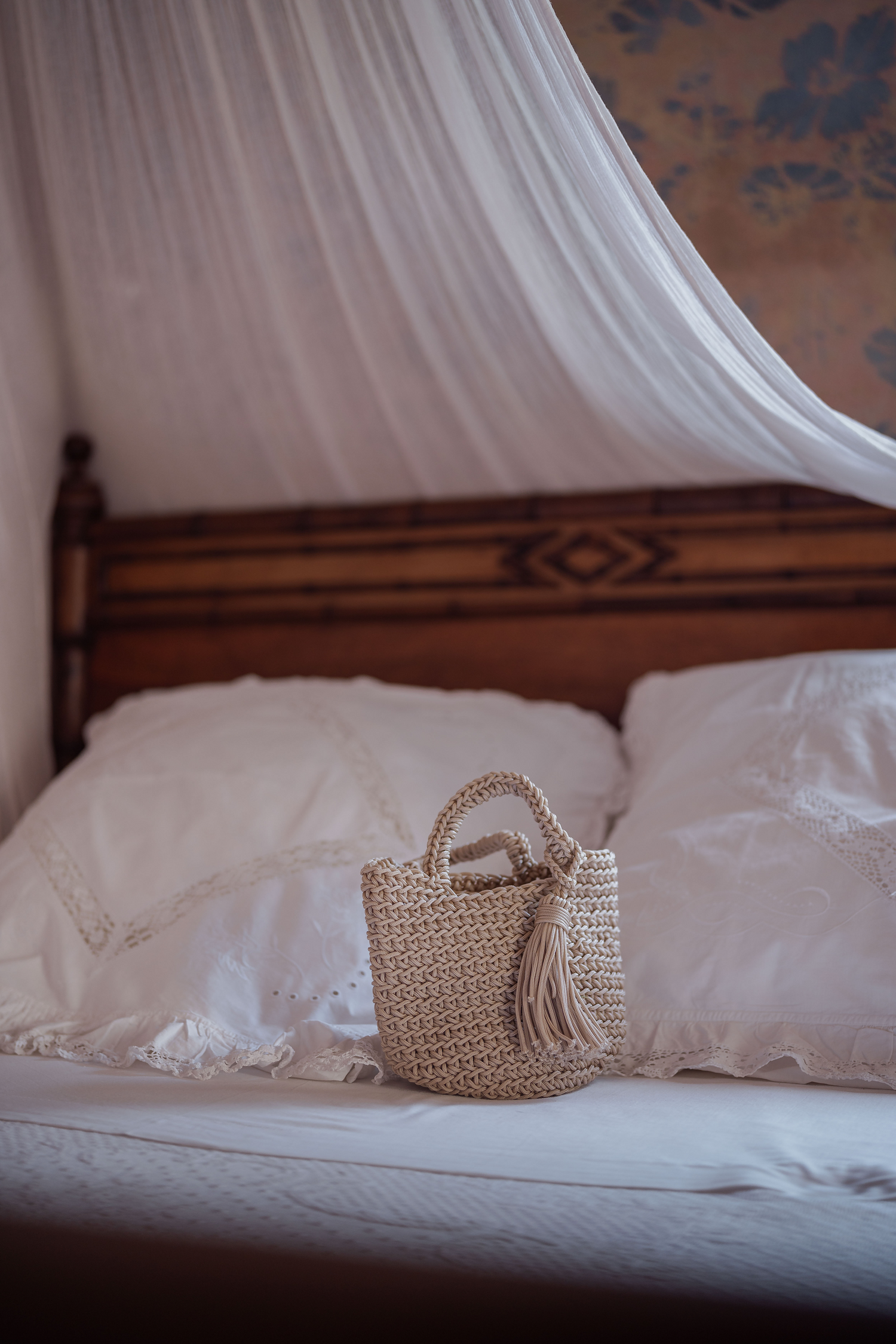 Mini borsa intrecciata a mano Marika Selection modello Sorrento beige con nappa tono su tono appoggiata su letto, accessorio chic artigianale.